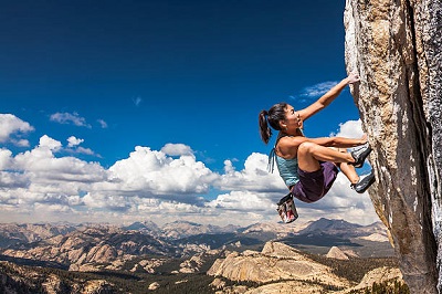Female climber dangles from the edge of a challenging cliff.